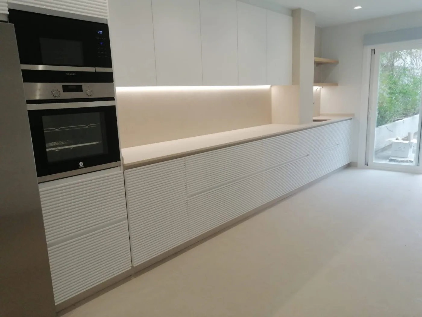 Cocina blanca con frentes estriados, iluminación integrada y horno en columna
